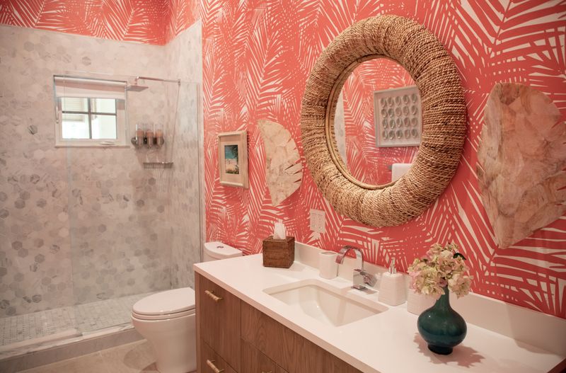 A bathroom in Harbour Island with coral palm print wallpaper and a round rope mirror over a white quartz vanity.