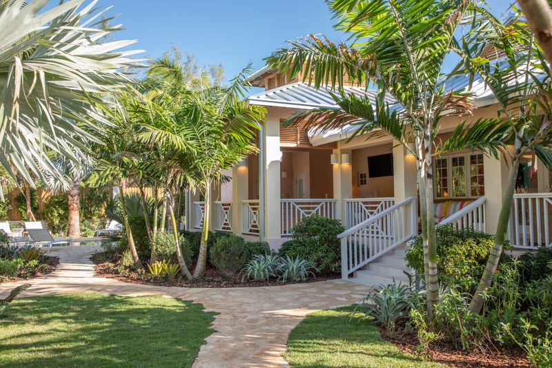 A covered porch in Harbour Island with white lattice railings under a standing seam metal roof, off a stone path.