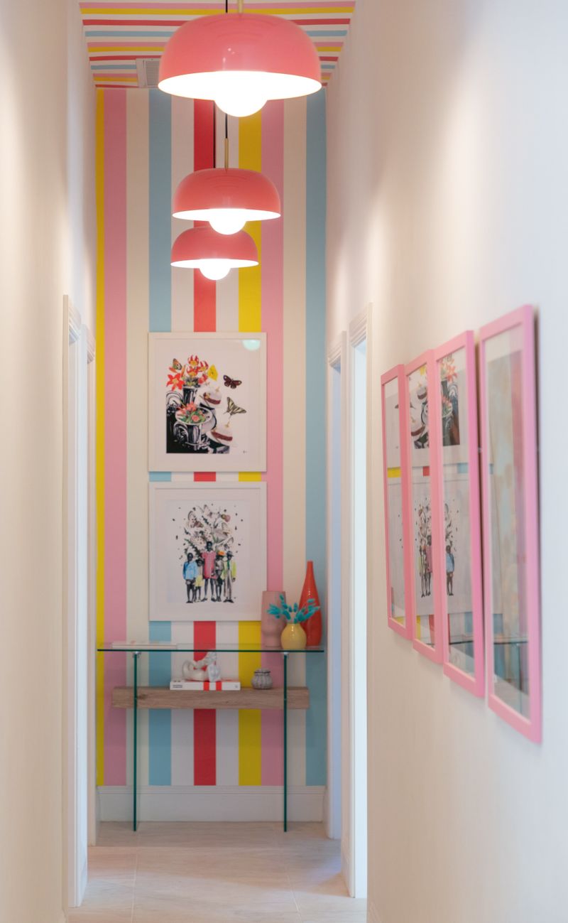 A hallway in Harbour Island with striped pink and yellow wallpaper under coral dome pendant lights.