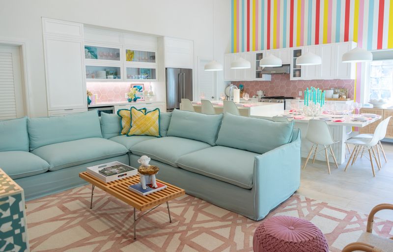 An open living room in Harbour Island with an aqua slipcovered sofa facing a kitchen with pink hexagon tile.