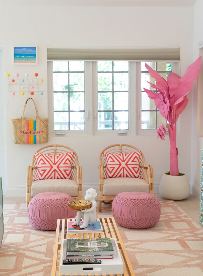 A white living room in Harbour Island with rattan chairs and pink poufs on a blush patterned rug.