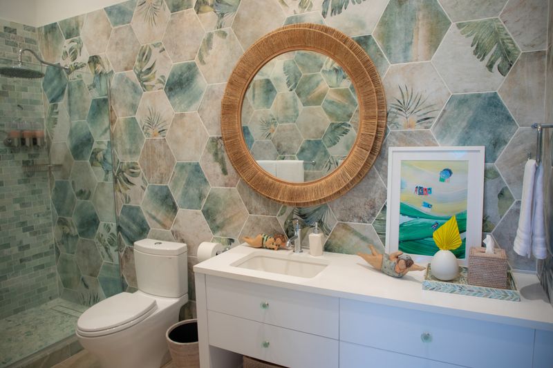 A powder room in Harbour Island with green palm print hexagon tile and a round rope mirror over a white vanity.