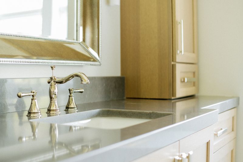 A bathroom vanity in Johnston with a polished brass widespread faucet on a grey stone countertop.