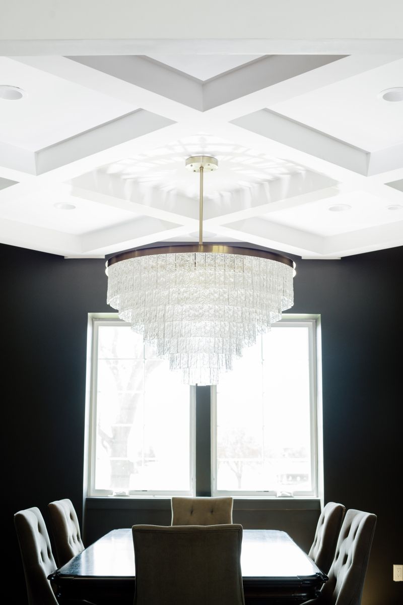 A black dining room in Johnston with a tiered glass chandelier under a white coffered ceiling.
