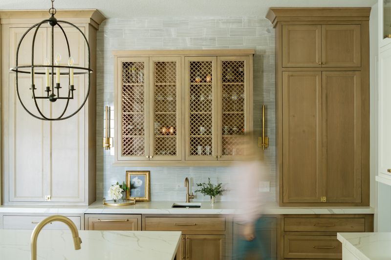 A light oak kitchen in Johnston with brass mesh cabinet doors above a white marble counter.