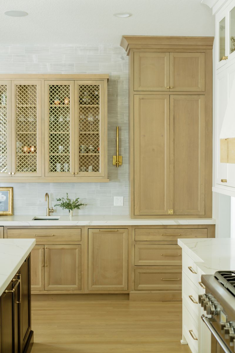 A white oak kitchen in Johnston with brass mesh cabinet doors above the bar sink and quartz counters.