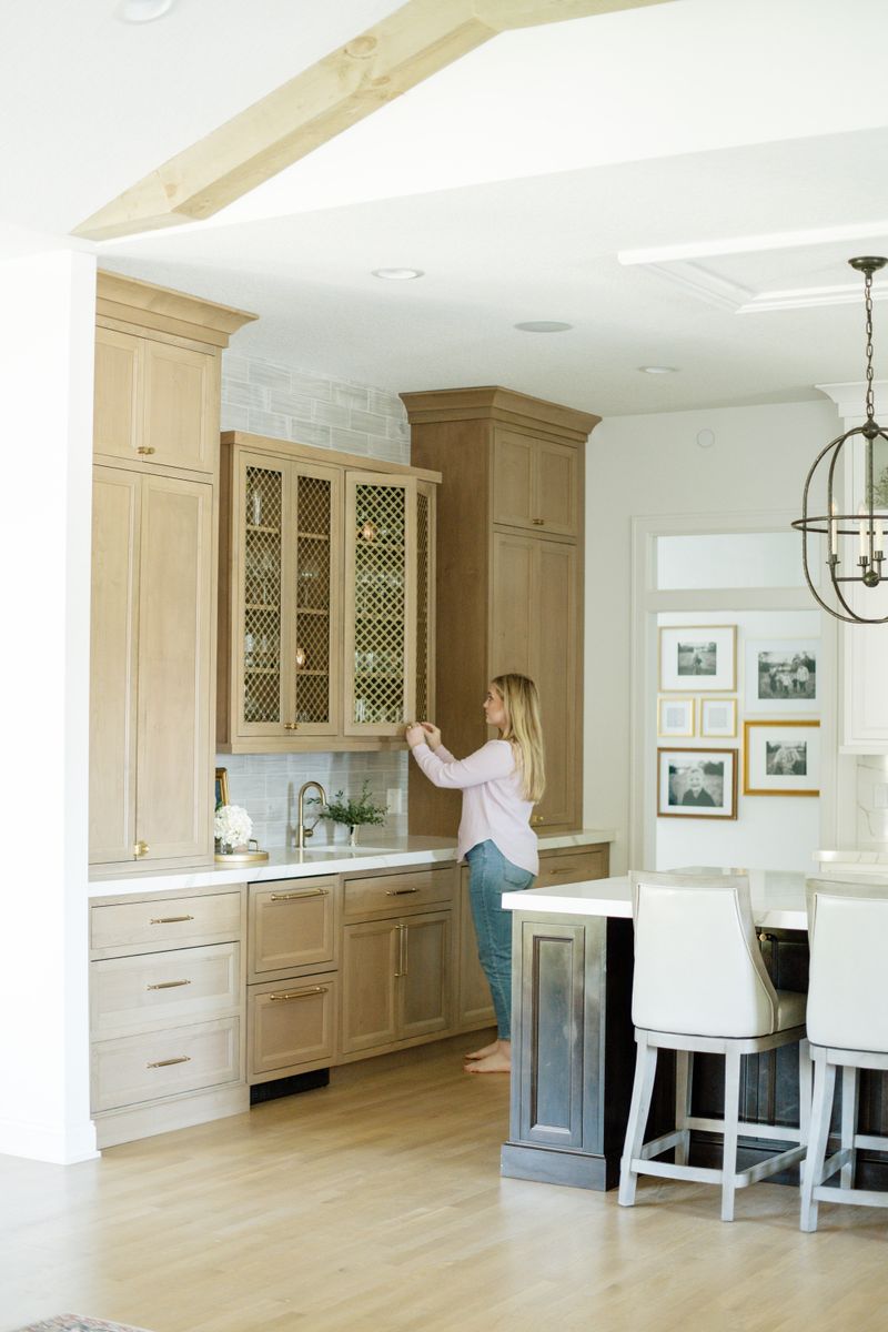 A light oak kitchen in Johnston with brass mesh cabinet doors above the sink and white marble counters.