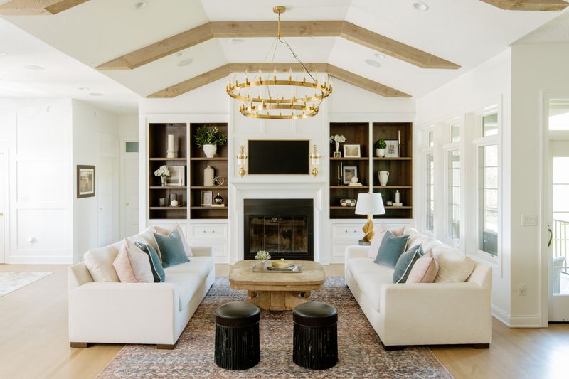 A white living room in Johnston with a brass two tier chandelier hung below wood ceiling beams.