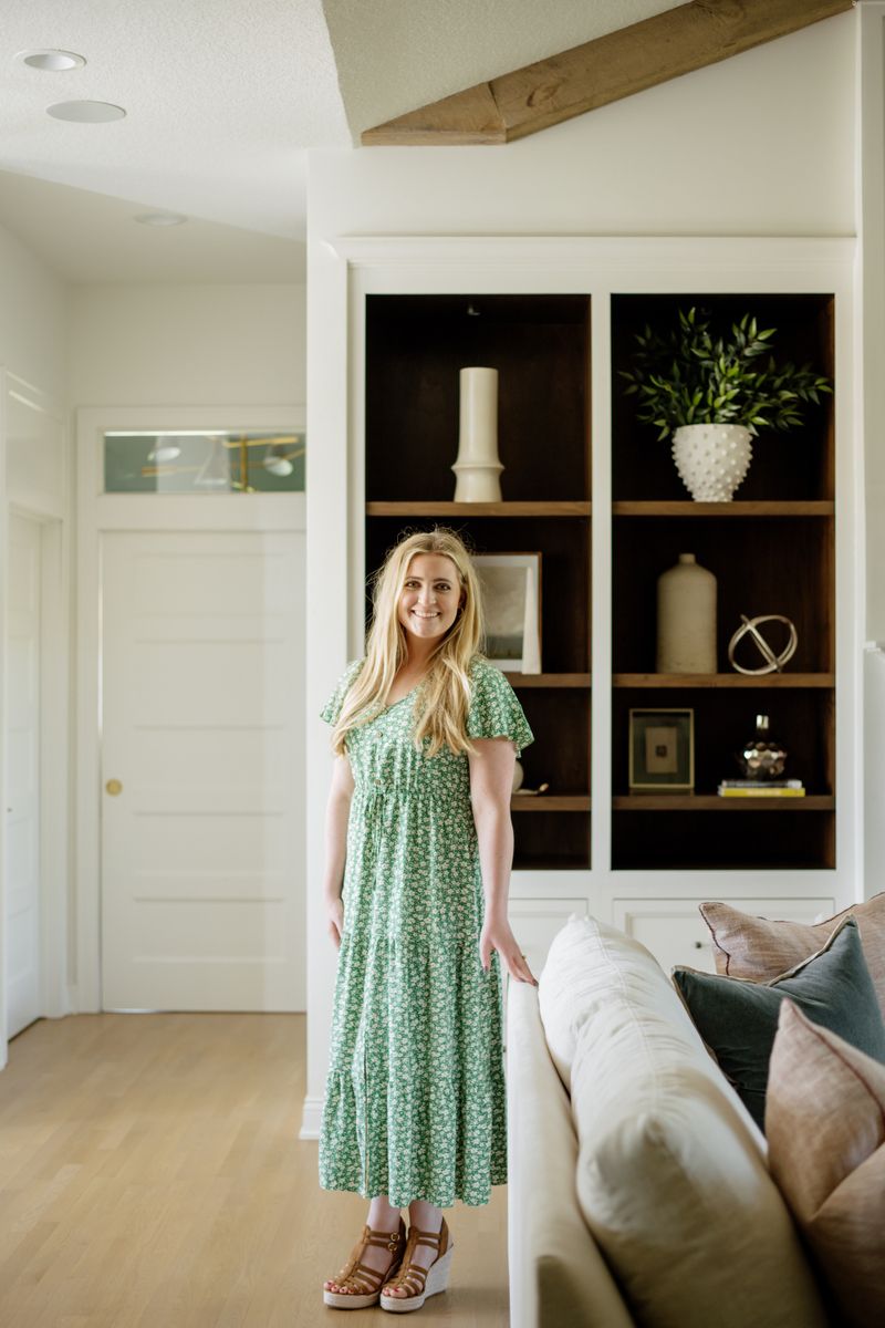 A designer standing in a Johnston living room with white built-ins and dark stained walnut shelves behind her.