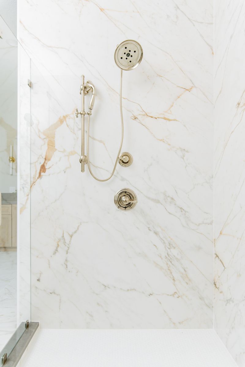 A primary bath shower in Johnston with polished nickel fixtures on a gold veined marble slab wall.