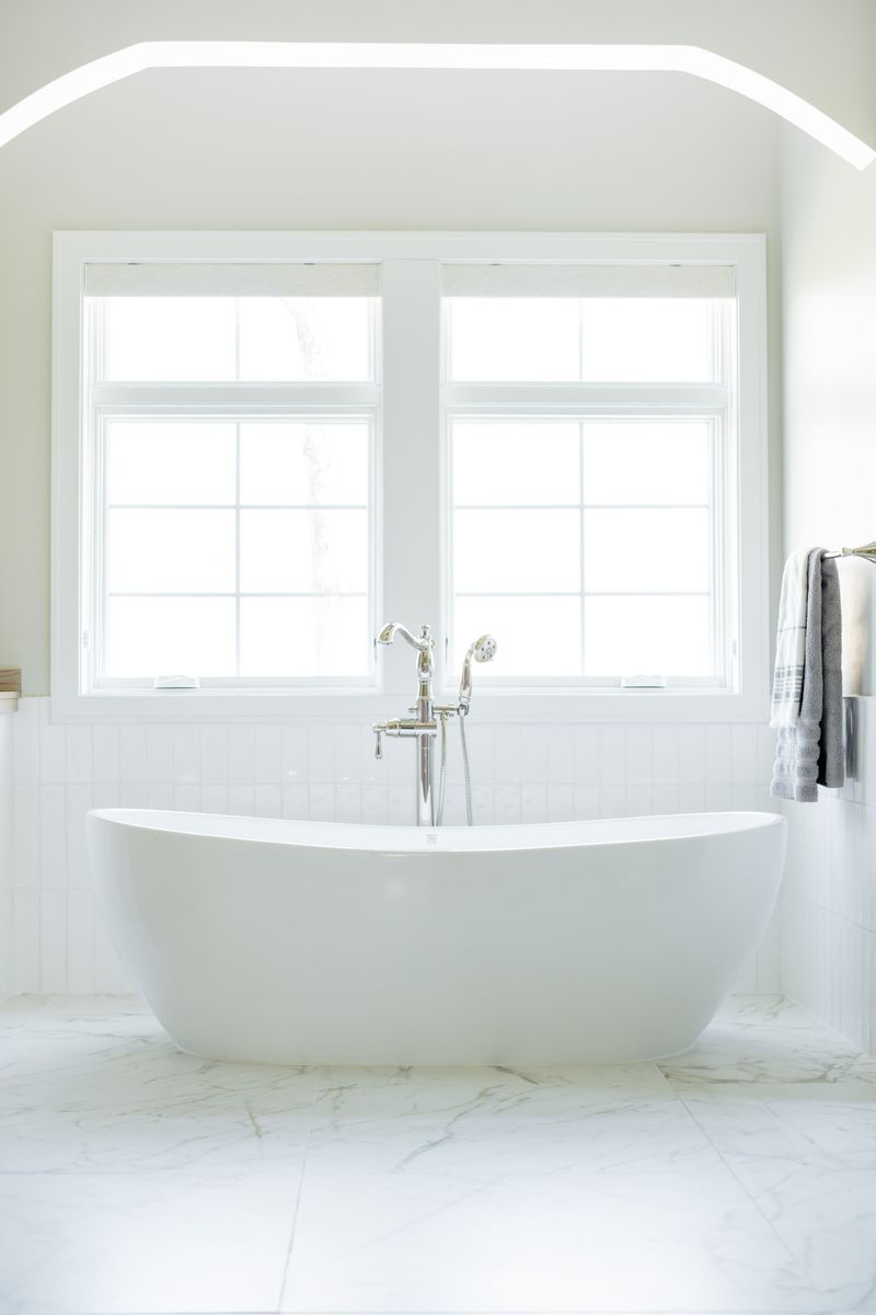 A white primary bath in Johnston with a freestanding soaking tub on marble tile and a chrome floor faucet.