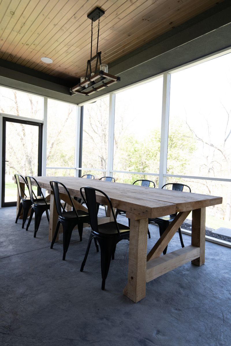 A screened porch in Johnston with a long reclaimed wood table and black metal chairs on a concrete floor.