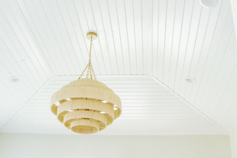 A tiered rope chandelier on a brass chain hanging from a white plank ceiling in Johnston.
