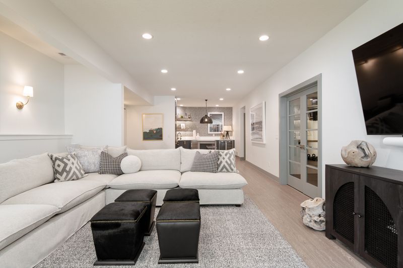 A finished basement in West Des Moines with black hide ottomans in front of a white sectional.