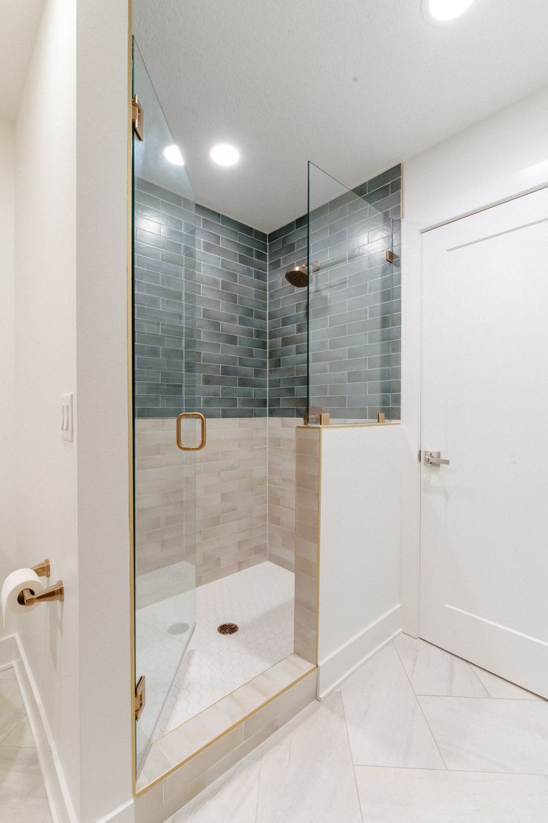 A white bathroom in West Des Moines with a two tone tiled shower in blue green and cream, framed in brass.