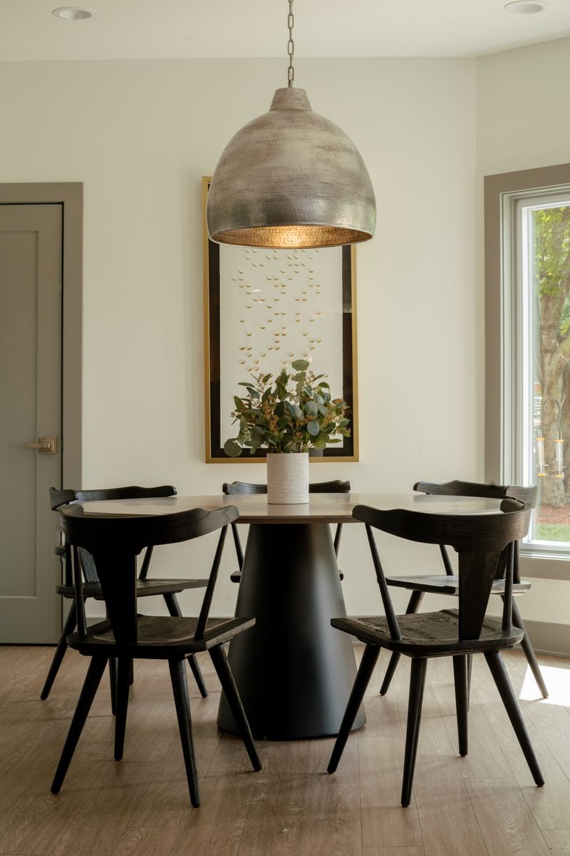A dining nook in West Des Moines with a hammered metal dome pendant over a round pedestal table and black wood chairs.