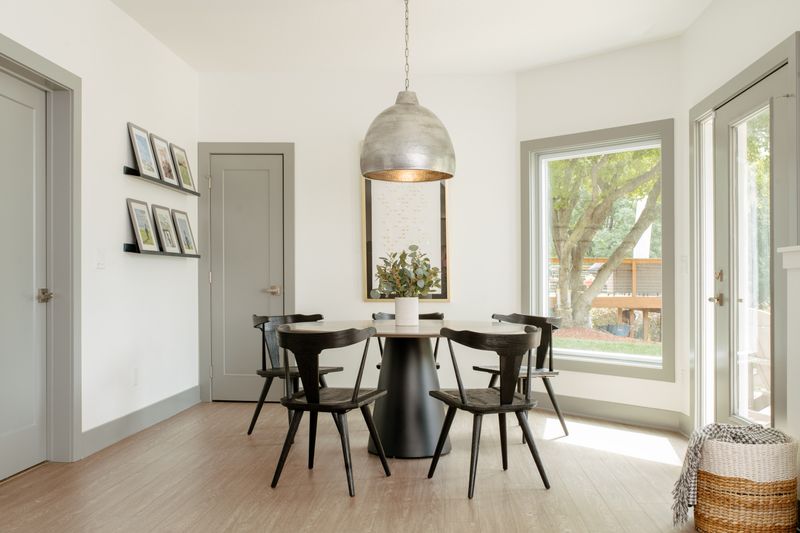 A white dining room in West Des Moines with an oversized metal dome pendant over a round black pedestal table.