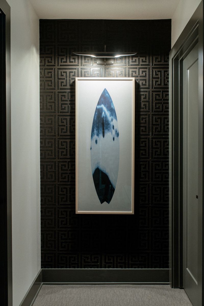 A hallway in West Des Moines with black Greek key wallpaper behind a framed blue surfboard print.