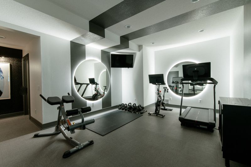A home gym in West Des Moines with round backlit mirrors on white and charcoal striped walls.