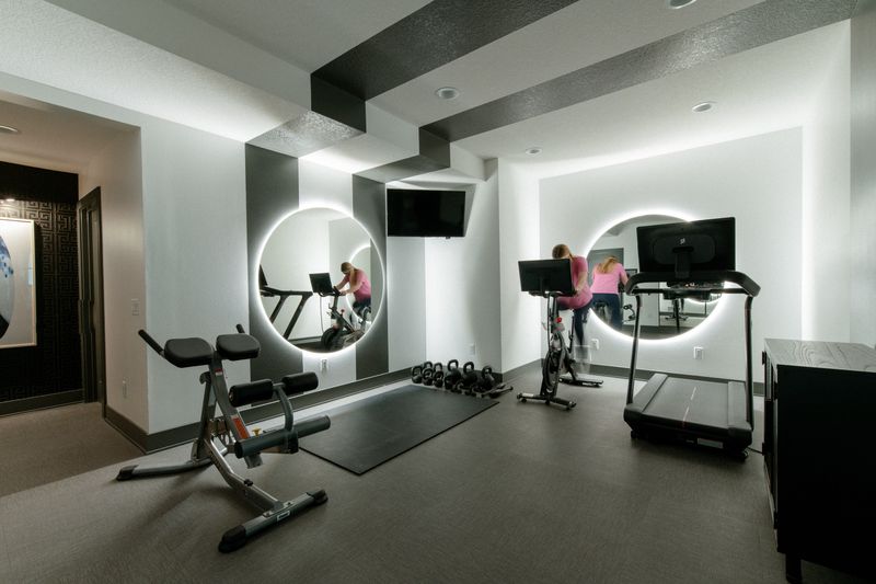 A black and white home gym in West Des Moines with round backlit mirrors above dark rubber flooring.