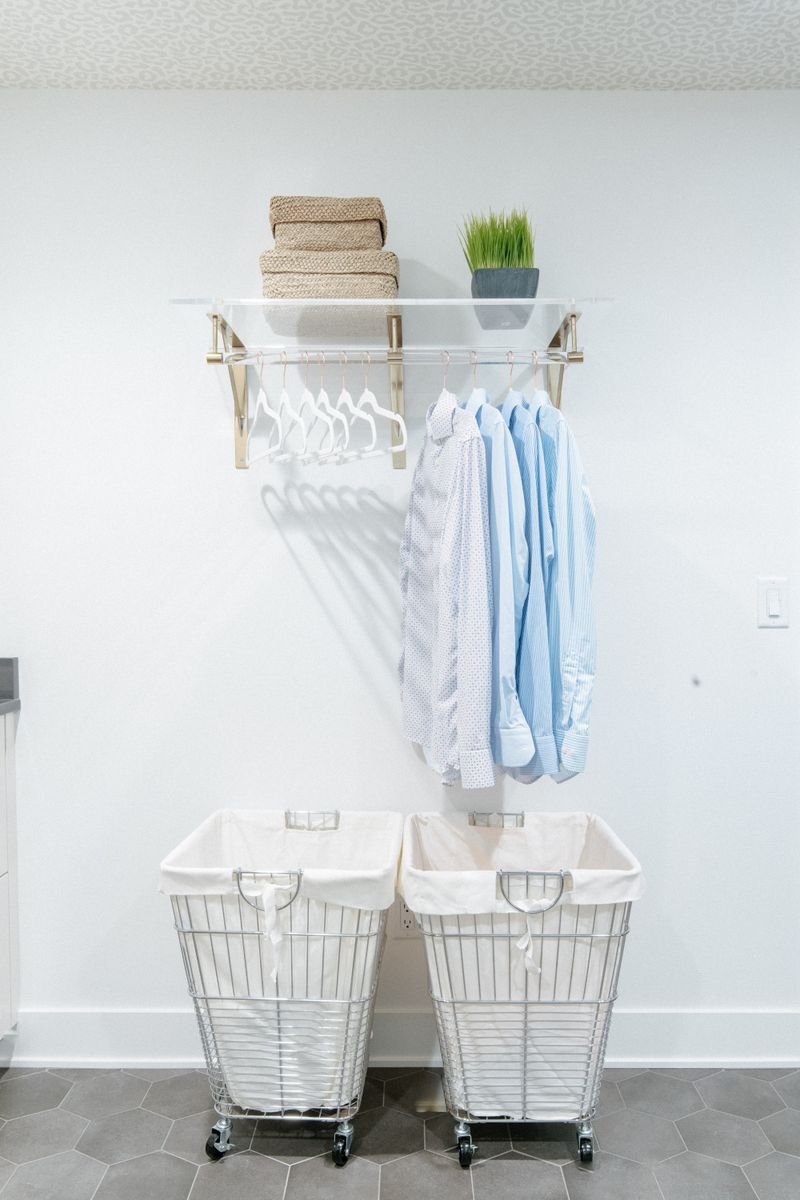 A white laundry room in West Des Moines with a brass and acrylic hanging rod above gray hexagon tile floors.