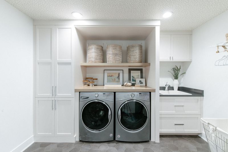 A white laundry room in West Des Moines with a dark gray quartz sink counter and gray hexagon tile floors.