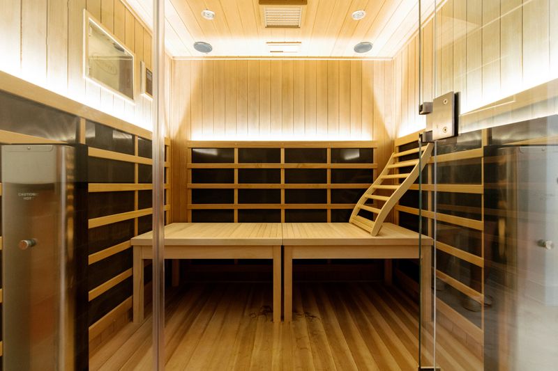 A cedar sauna in West Des Moines with a curved wood backrest on the bench and a glass door.
