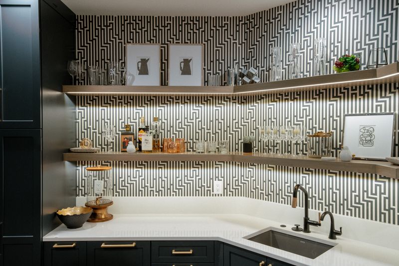 A wet bar in West Des Moines with black and white geometric wallpaper behind lit oak floating shelves.