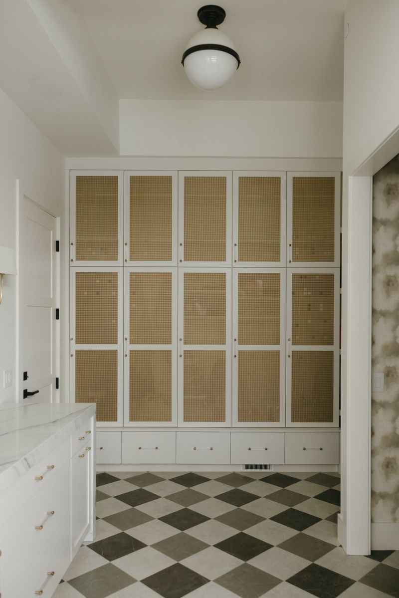 A butlers pantry in West Des Moines with brass mesh cabinet doors above a checkered marble floor.