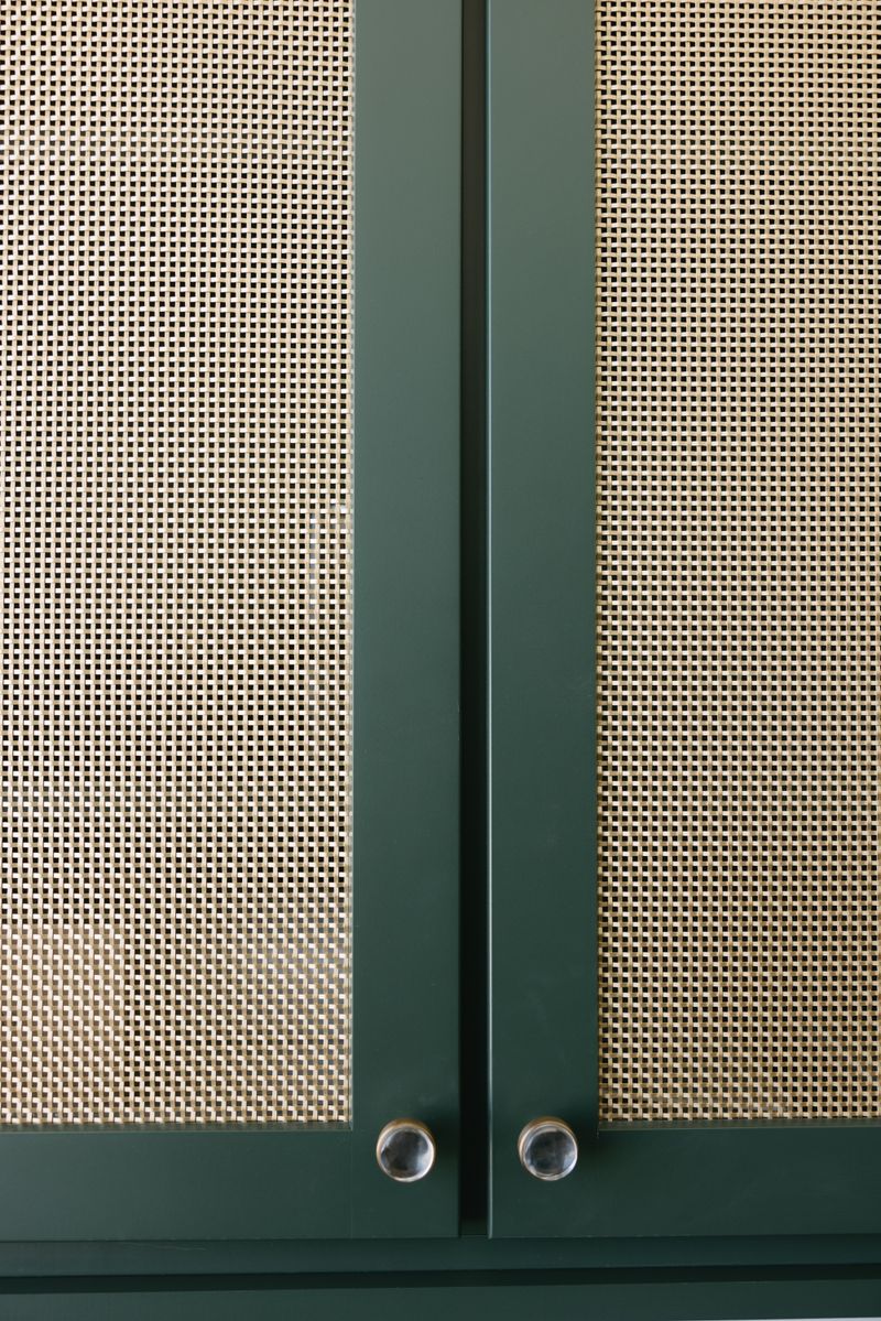 Dark green cabinet doors in West Des Moines with woven cane panels and round glass and brass knobs.