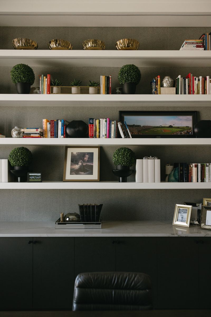 A home office in West Des Moines with white floating shelves over textured herringbone wallpaper and a marble desktop.