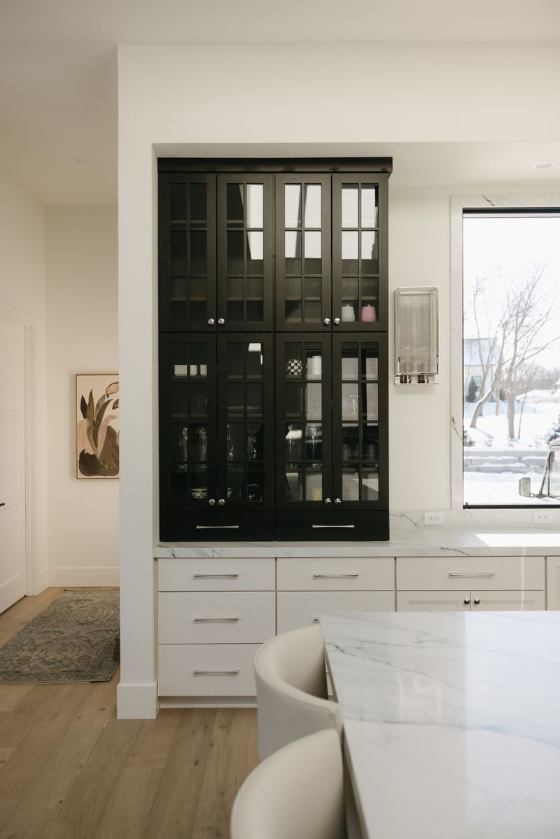A white kitchen in West Des Moines with a black glass front hutch above marble counters.