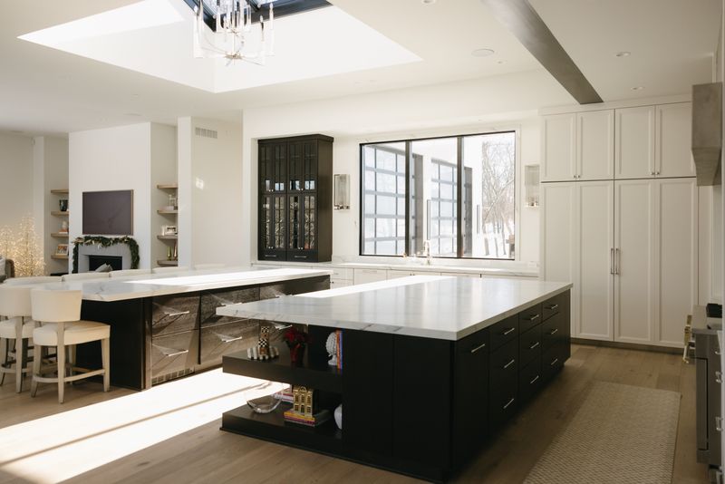 A white kitchen in West Des Moines with a marble waterfall counter on a black island over pale oak floors.