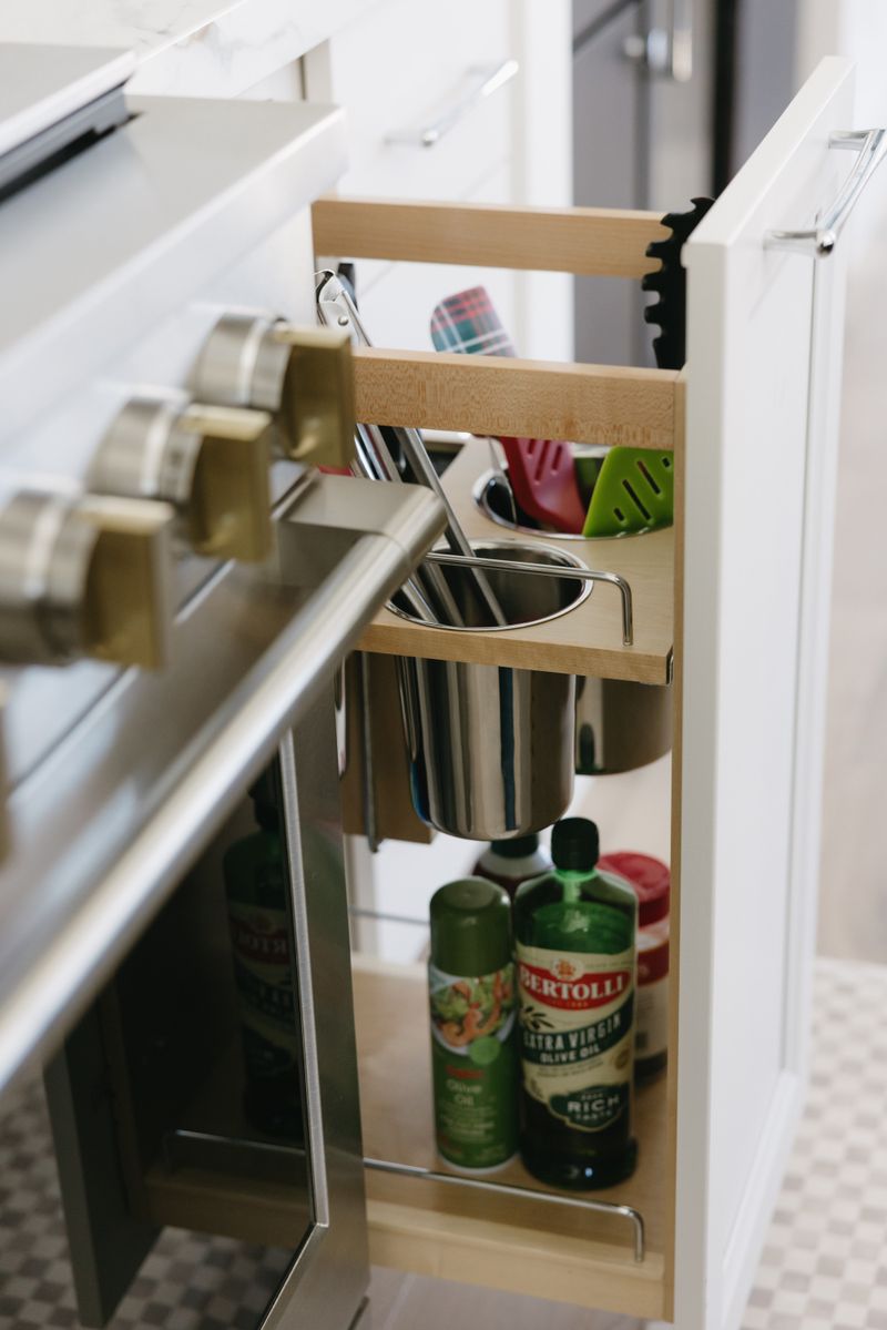 A white kitchen in West Des Moines with a maple pull-out pantry beside the range, holding oils and utensils.