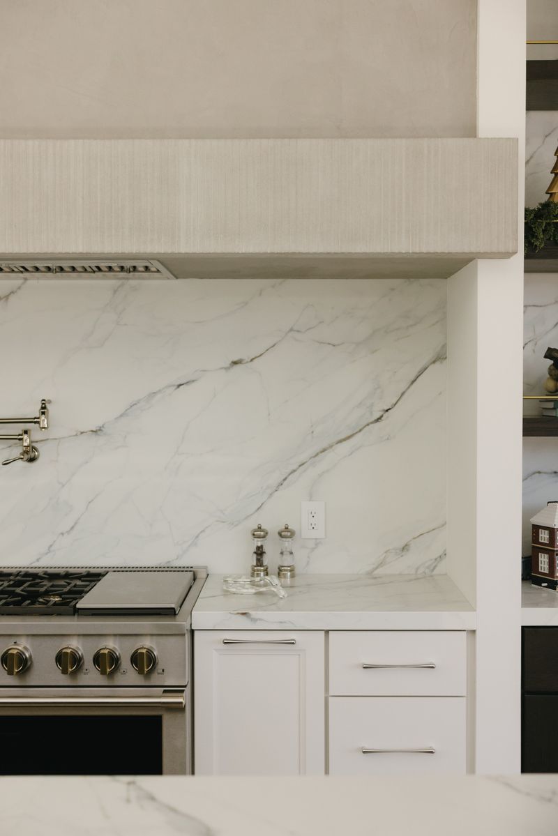 A white kitchen in West Des Moines with a marble slab backsplash behind the range and a plaster hood above.