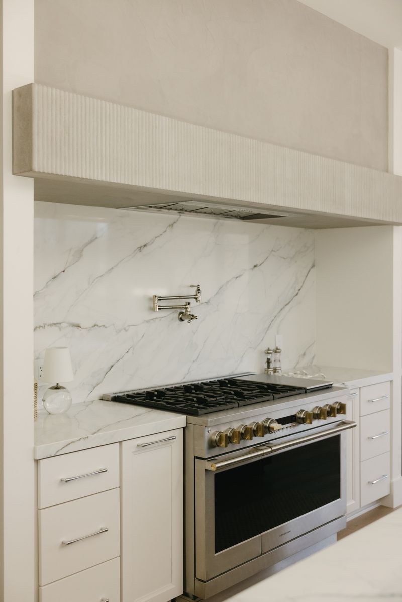 A cream kitchen in West Des Moines with a marble slab backsplash behind a stainless range and pot filler.