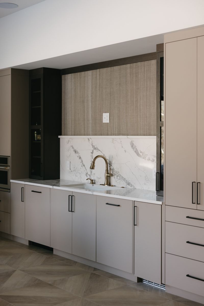 A greige kitchen in West Des Moines with a brass faucet against a marble slab backsplash.