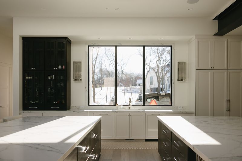 A white kitchen in West Des Moines with a marble slab backsplash running up behind a black framed window.