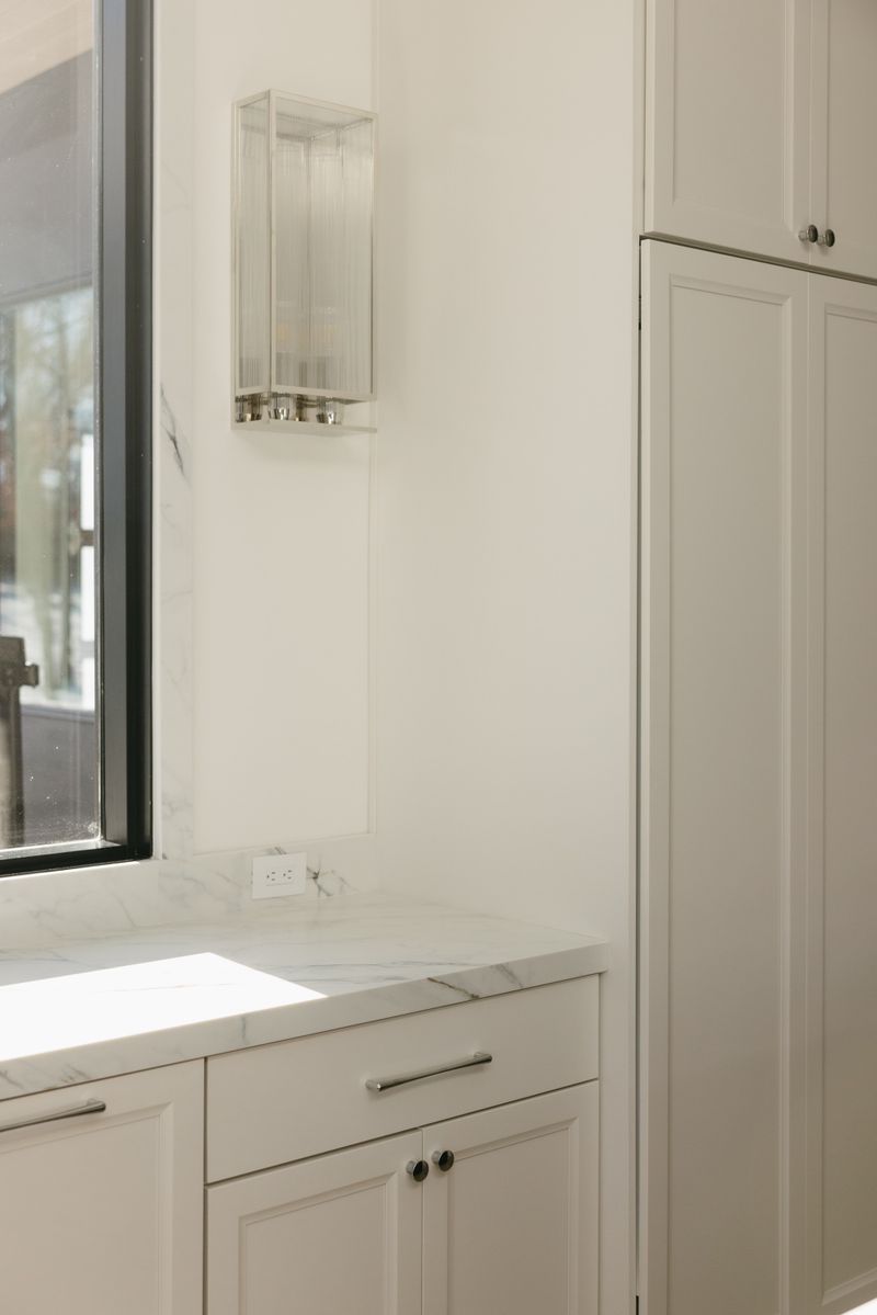 A white kitchen in West Des Moines with a marble counter and backsplash beside a black framed window.