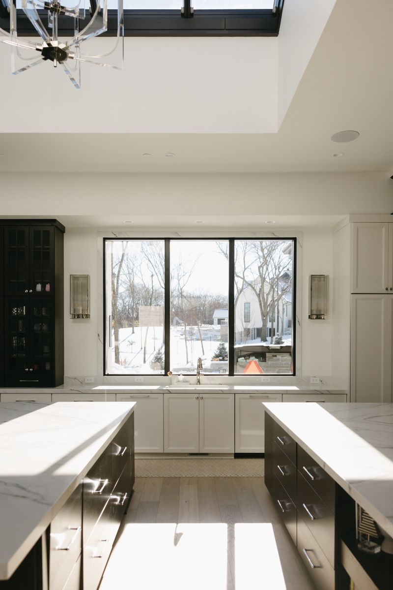 A white kitchen in West Des Moines with twin dark wood islands under marble waterfall counters.
