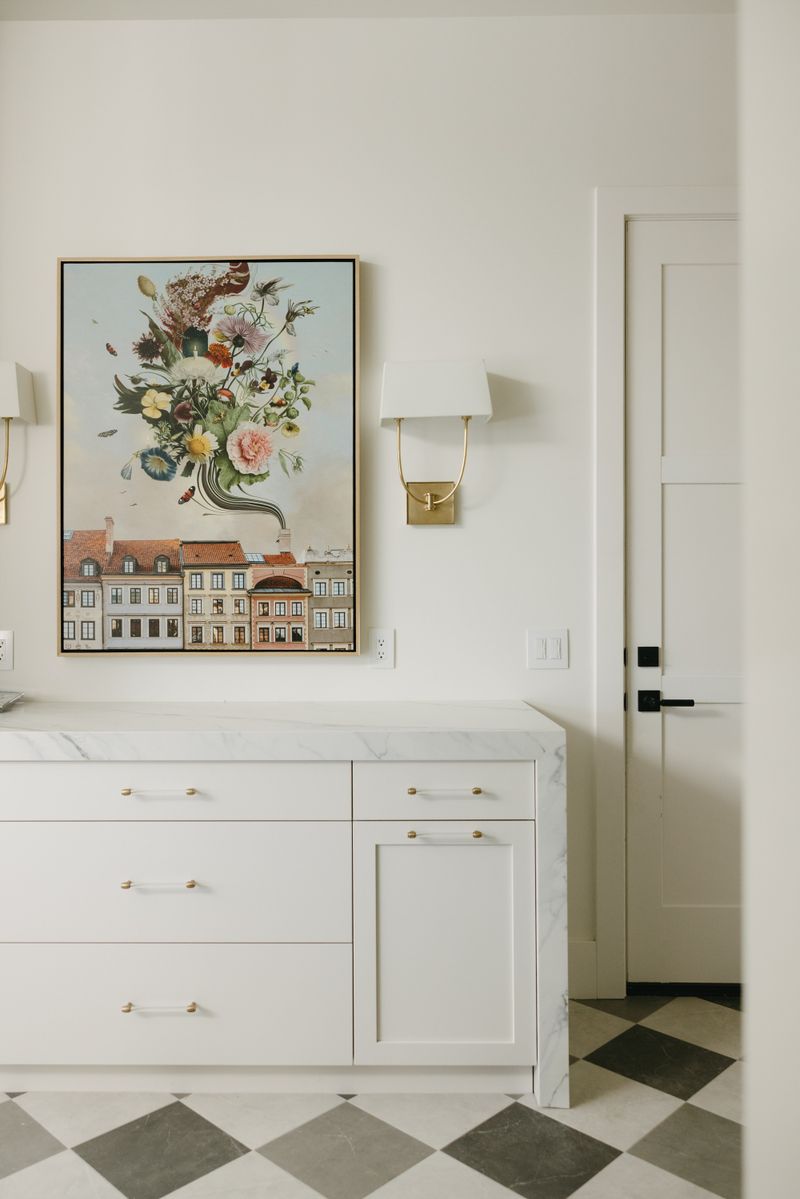 A white kitchen in West Des Moines with a brass sconce above a marble waterfall counter.
