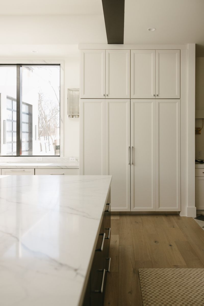 A white kitchen in West Des Moines with a floor to ceiling paneled pantry wall beside a marble island.