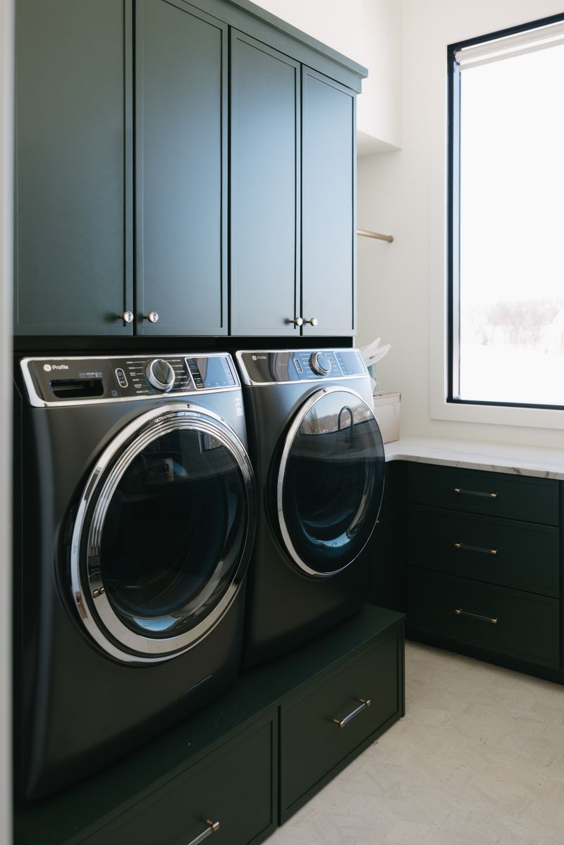 A laundry room in West Des Moines with deep green cabinets above the washer and dryer and brass drawer pulls.