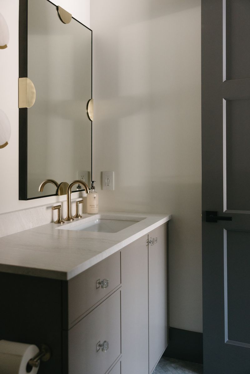 A powder room in West Des Moines with a brass faucet on a marble vanity top over gray cabinets.