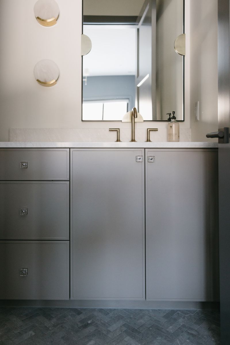 A powder room in West Des Moines with a gray vanity and a brass faucet on a white marble counter.