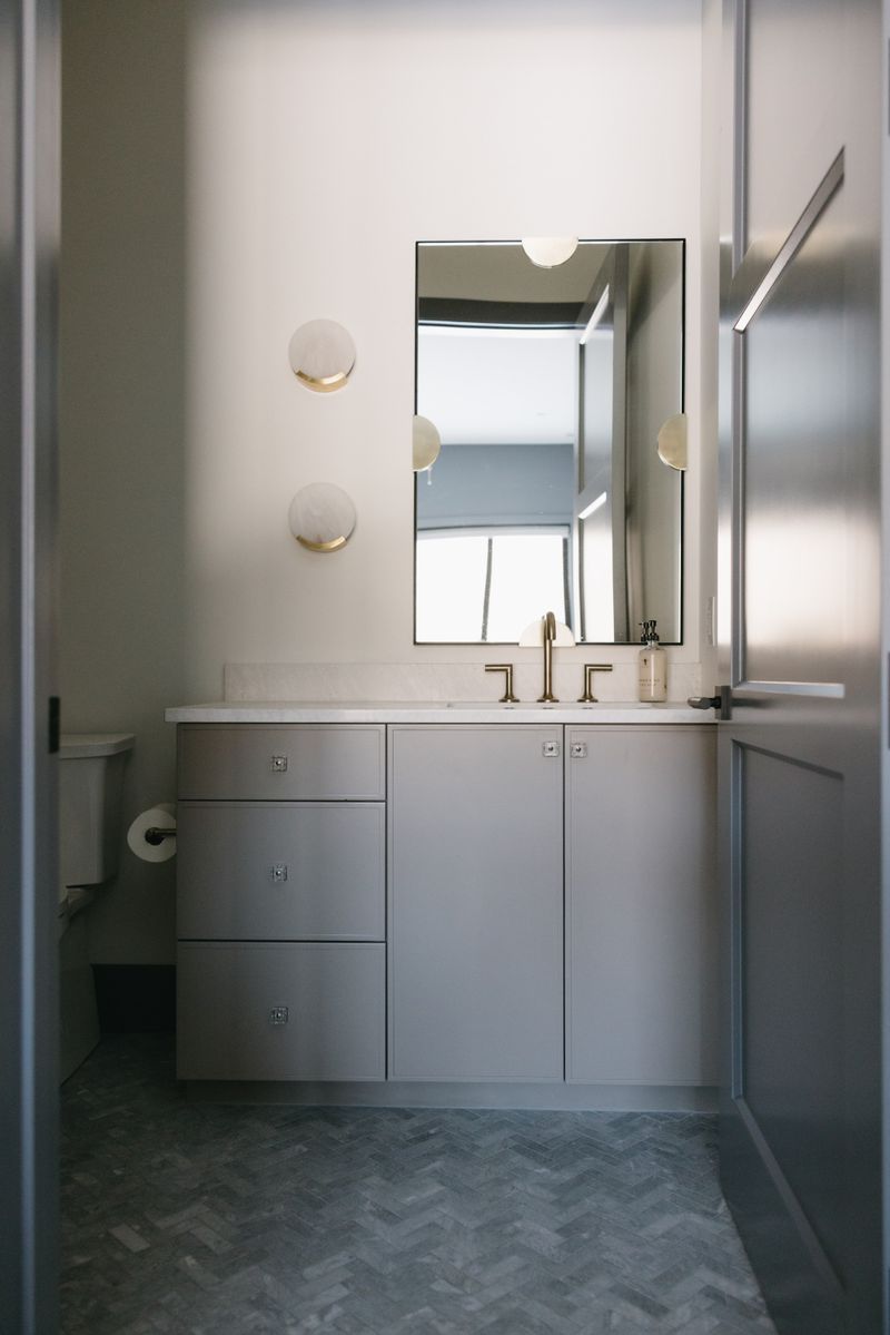 A powder room in West Des Moines with alabaster and brass sconces above a gray vanity topped in white marble.
