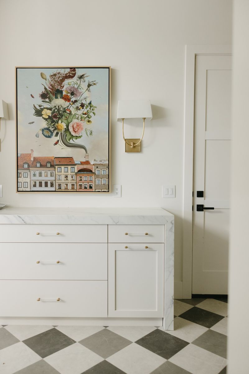 A primary bath in West Des Moines with a brass sconce above white vanity cabinets and a marble waterfall counter.