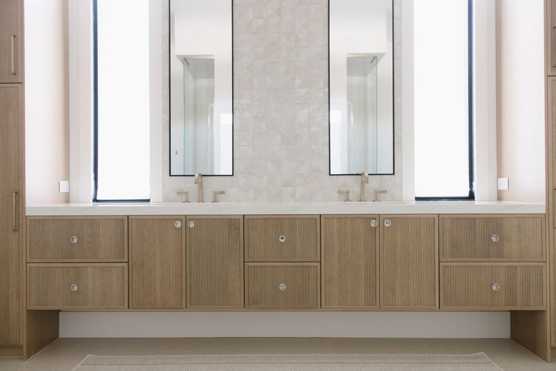 A primary bath in West Des Moines with a fluted white oak vanity under a brass wall-mount faucet.