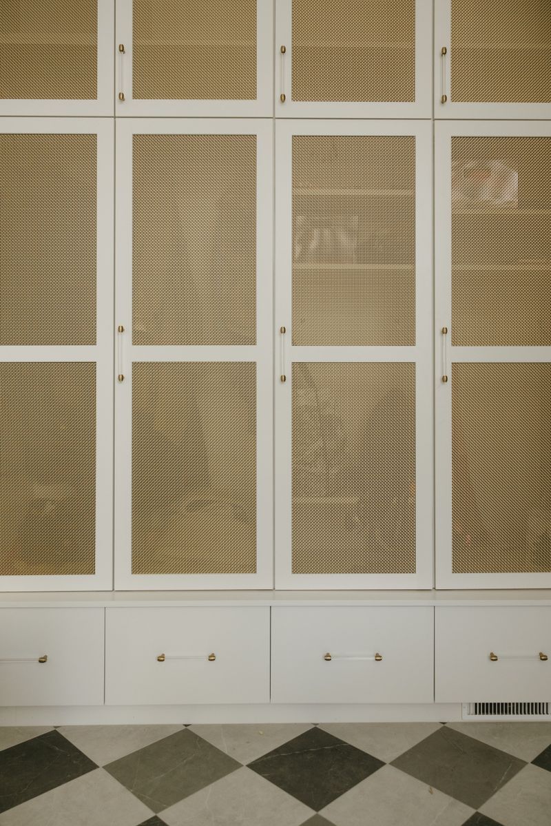 A walk in closet in West Des Moines with brass mesh panels set into white cabinet doors and lucite pulls.