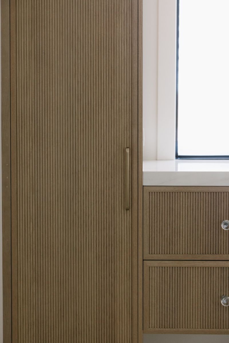 A walk in closet in West Des Moines with fluted oak cabinet doors and a brass pull by the window.